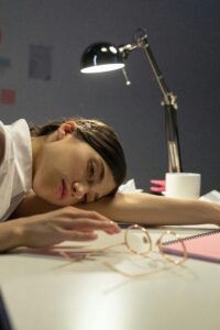 Tired woman resting head on desk with a lamp, representing stress and exhaustion.